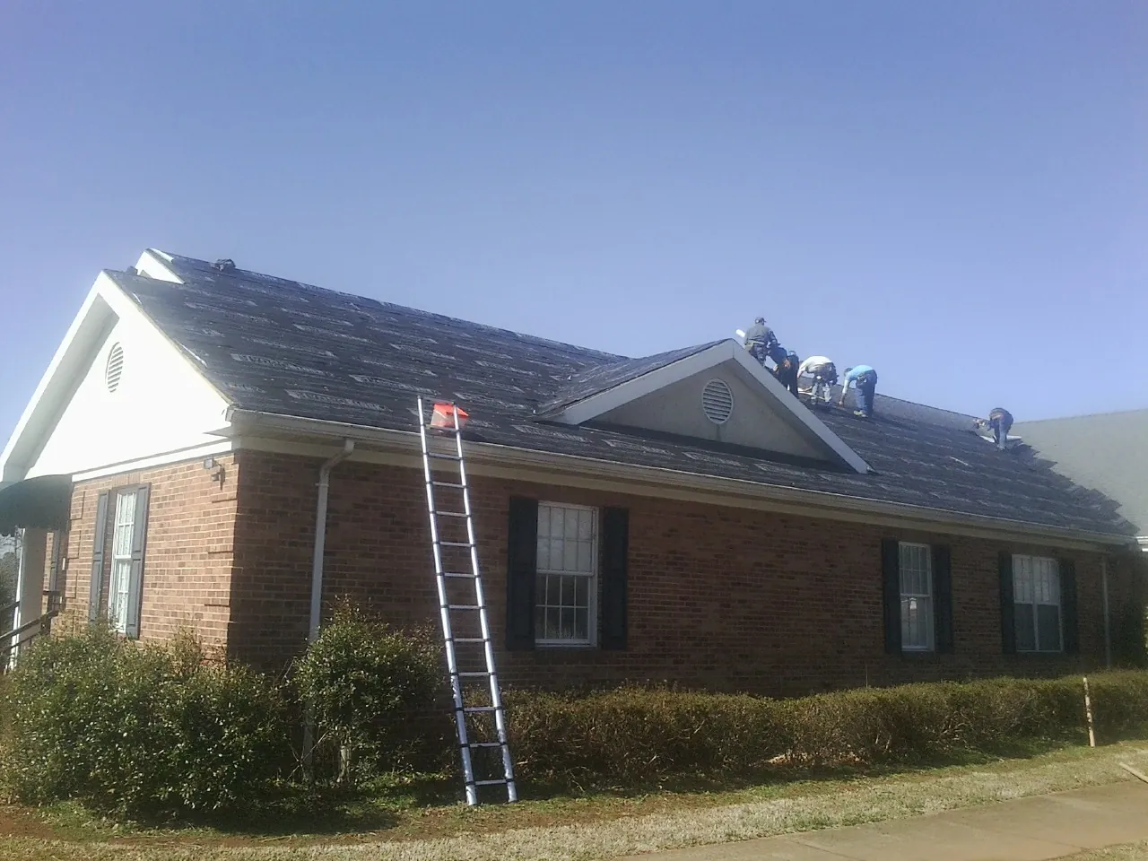 Crew tearing shingles off a brick ranch roof with a ladder set — Metal Roof Repair work by our crew in Waring