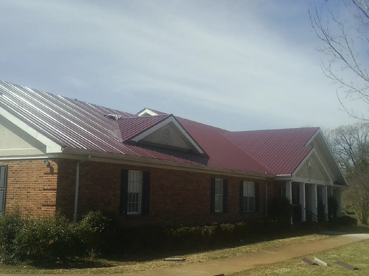 Red metal roof with gabled entries on a long brick building, from a Hail Damage Roof Repair job in Waring