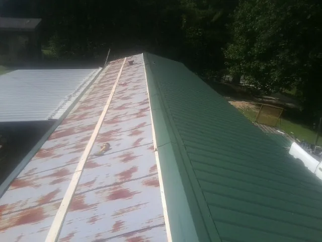 Old rusted panels beside newly installed green metal roofing — Wind Damage Roof Repair by Roofing Brothers in Waring