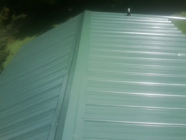 New green metal panels meeting at the ridge of a roof — Flat Roof Repair work by our crew in Waring
