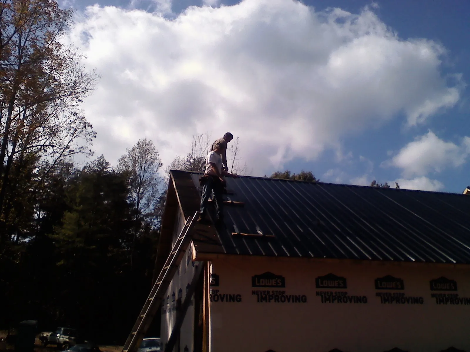 Roofer fastening dark metal panels high against a cloudy sky, from a Roof Inspection job in Waring
