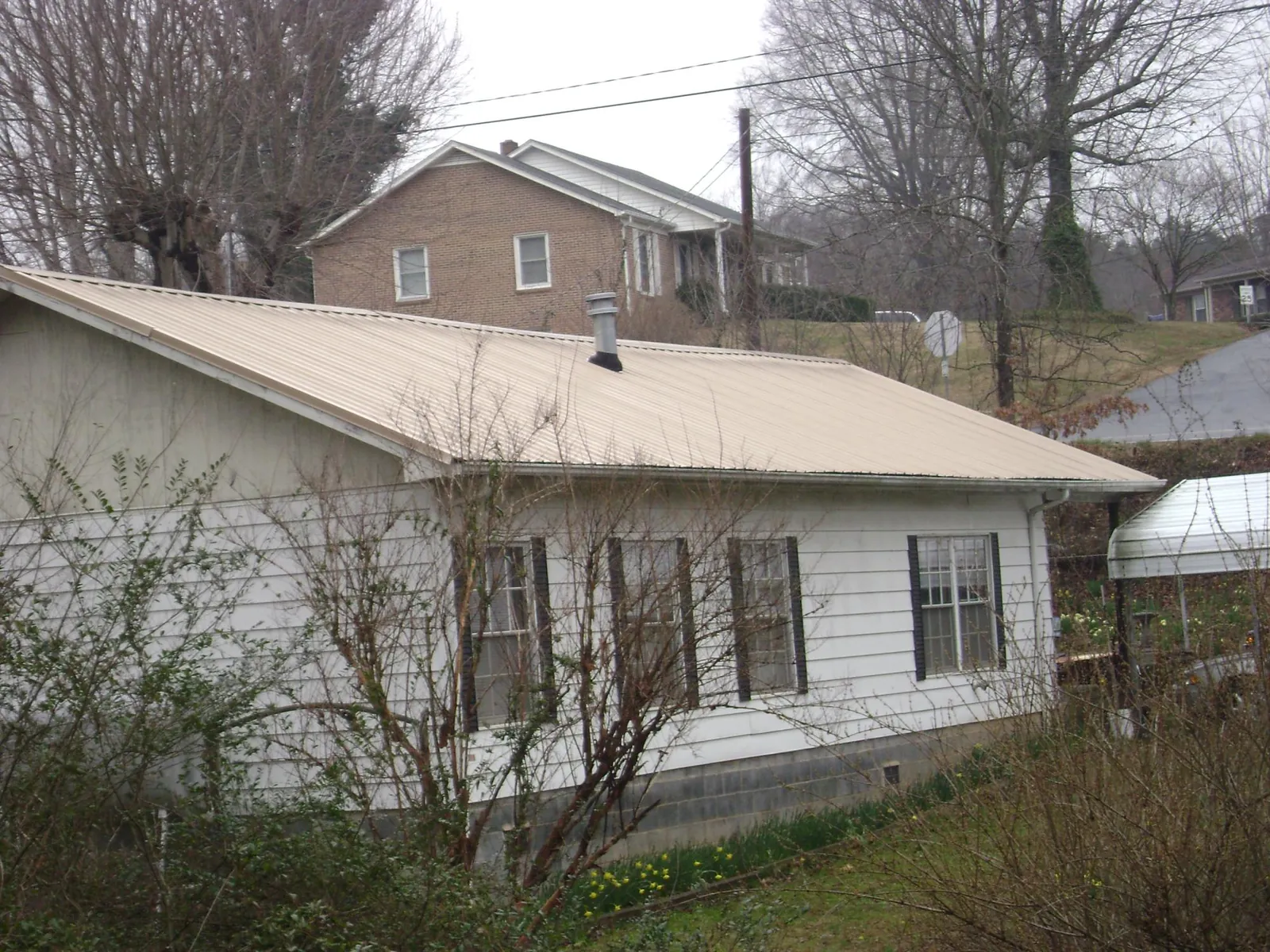 Tan metal roof on a white sided house set into a hillside — Commercial Roofing by Roofing Brothers in Waring